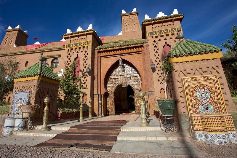 Entrée de la villa Lakasbah à Marrakech, avec son portail en arc mauresque sculpté, ses zellige colorés et ses tapis berbères devant l'entrée