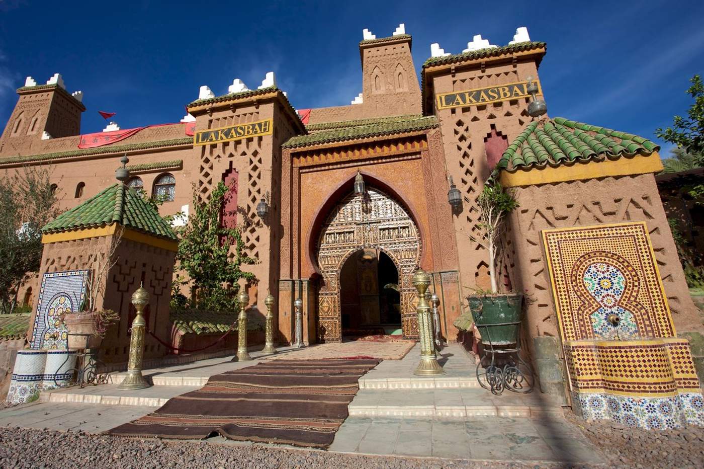 Entrée de la villa Lakasbah à Marrakech, avec son portail en arc mauresque sculpté, ses zellige colorés et ses tapis berbères devant l'entrée