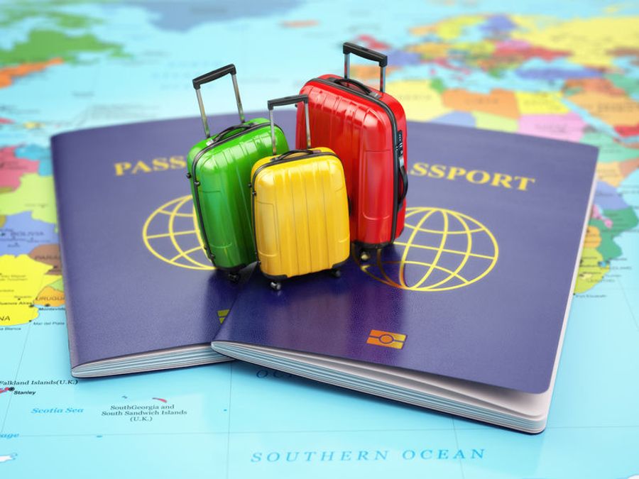 Trois petites valises de couleurs vert, jaune et rouge posées sur des passeports, symbolisant la préparation des documents et des affaires nécessaires pour un voyage en Croatie, avec une carte du monde en arrière-plan.