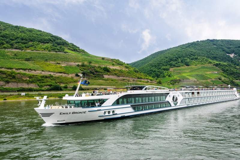 Bateau de croisière naviguant sur le Rhin, entouré de collines verdoyantes et de vignobles en terrasses dans la vallée du Rhin romantique.