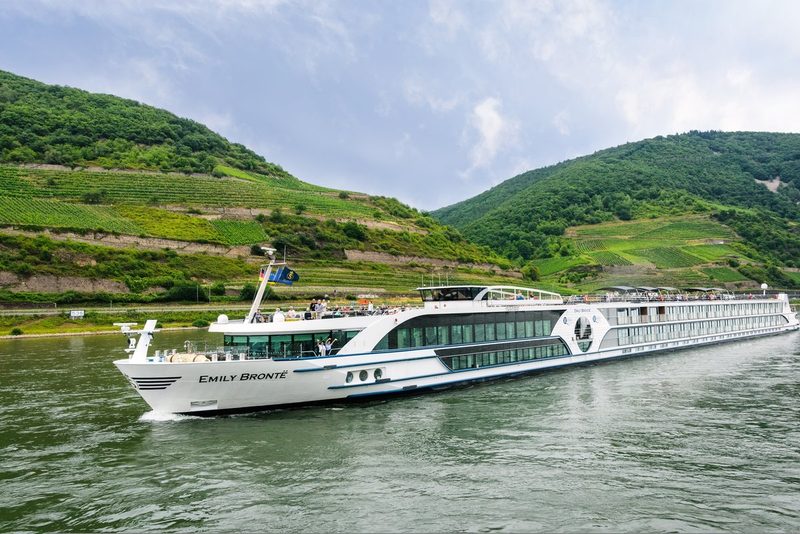 Bateau de croisière naviguant sur le Rhin, entouré de collines verdoyantes et de vignobles en terrasses dans la vallée du Rhin romantique.