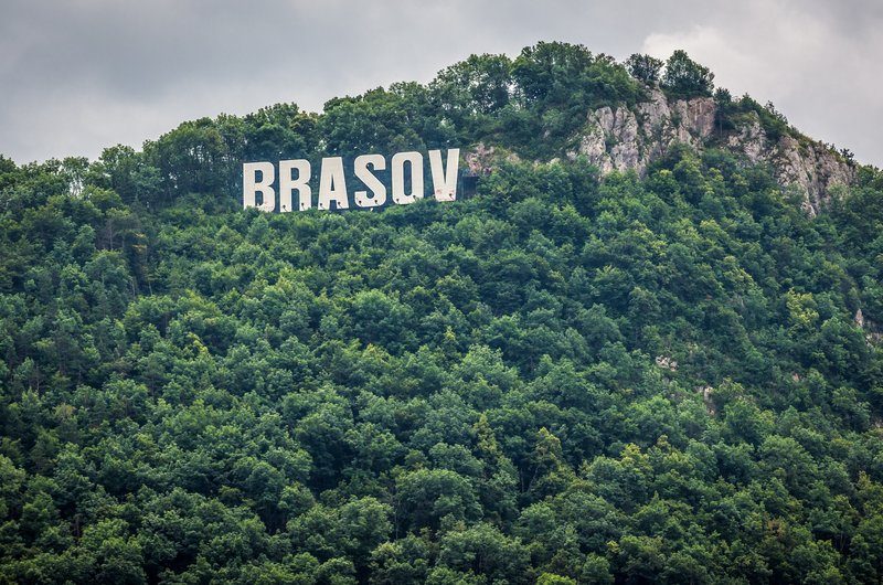 Vue sur le panneau "Brașov" style Hollywood sur le Mont Tâmpa, avec une dense forêt en arrière-plan.