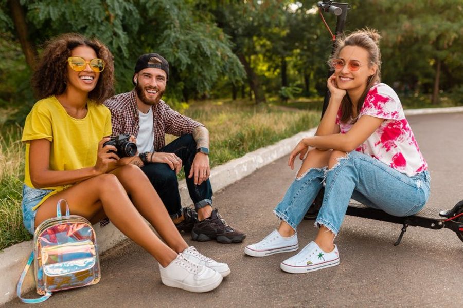 Trois amis souriants assis dans un parc avec un appareil photo et un sac à dos holographique, prêts pour un road trip