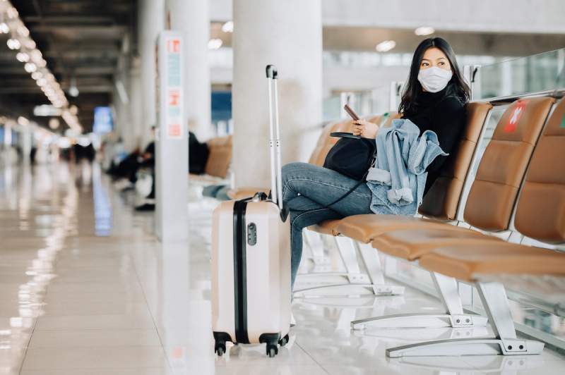 Une femme assise avec un masque de protection à l'aéroport