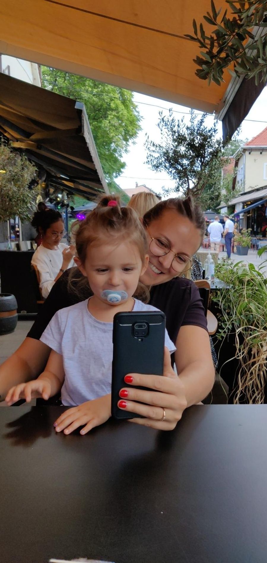 Maud souriante tenant Anna sur ses genoux, en conversation vidéo devant le téléphone.