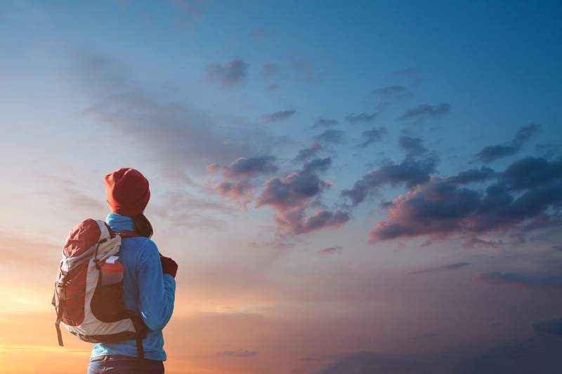Personne portant un sac à dos regardant un ciel coloré au coucher du soleil.
