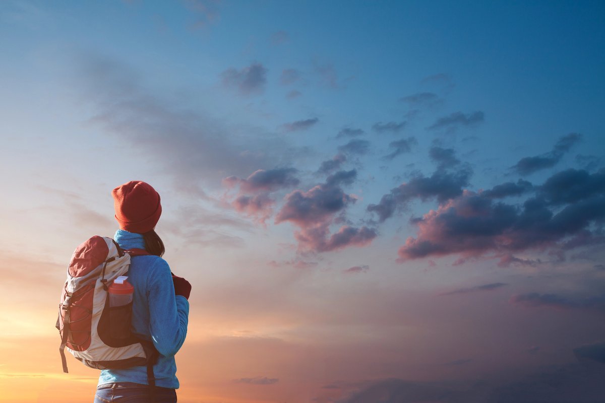 Personne portant un sac à dos regardant un ciel coloré au coucher du soleil.