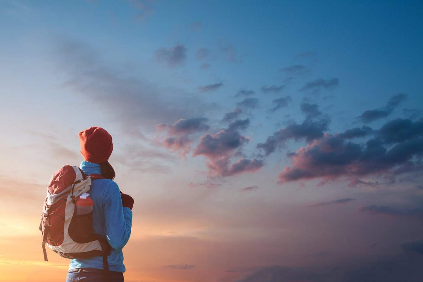 Personne portant un sac à dos regardant un ciel coloré au coucher du soleil.