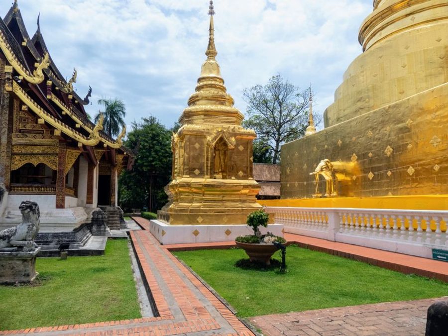 Temple doré à Wat Phra Singh avec des détails architecturaux complexes et un ciel nuageux.