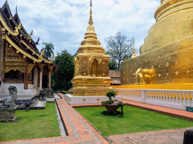 Temple doré à Wat Phra Singh avec des détails architecturaux complexes et un ciel nuageux.