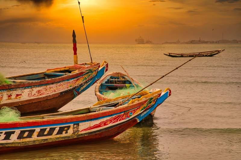 Pirogues colorées sur la côte d’Afrique de l’Ouest au coucher du soleil avec filet de pêche et mer calme