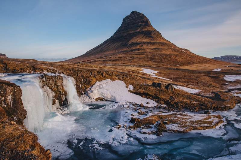 Vue sur la montagne Kirkjufell et les chutes gelées de Kirkjufellsfoss en Islande, photographiées en hiver avec des zones de glace et de neige.