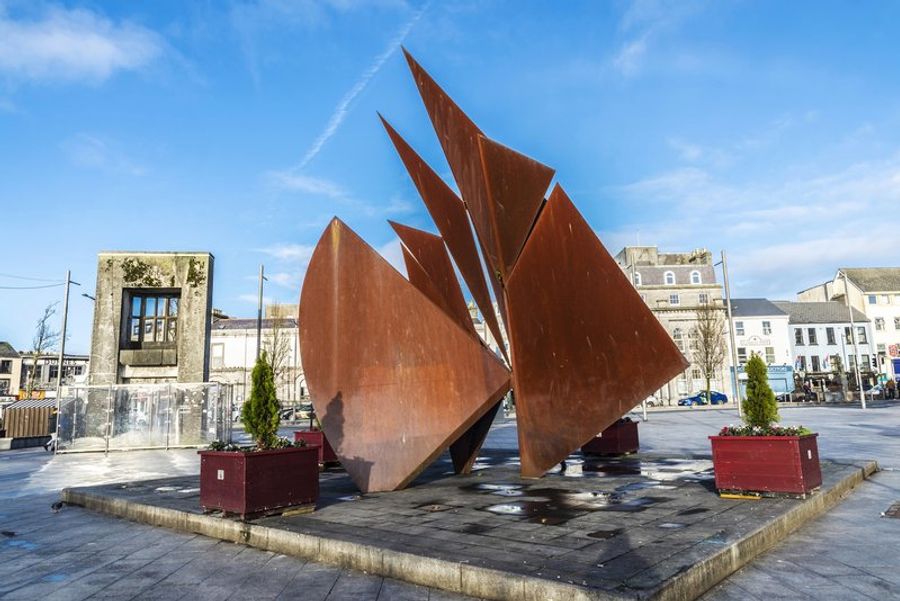 Sculpture moderne sur Eyre Square, un lieu central à Galway entouré de bâtiments historiques.