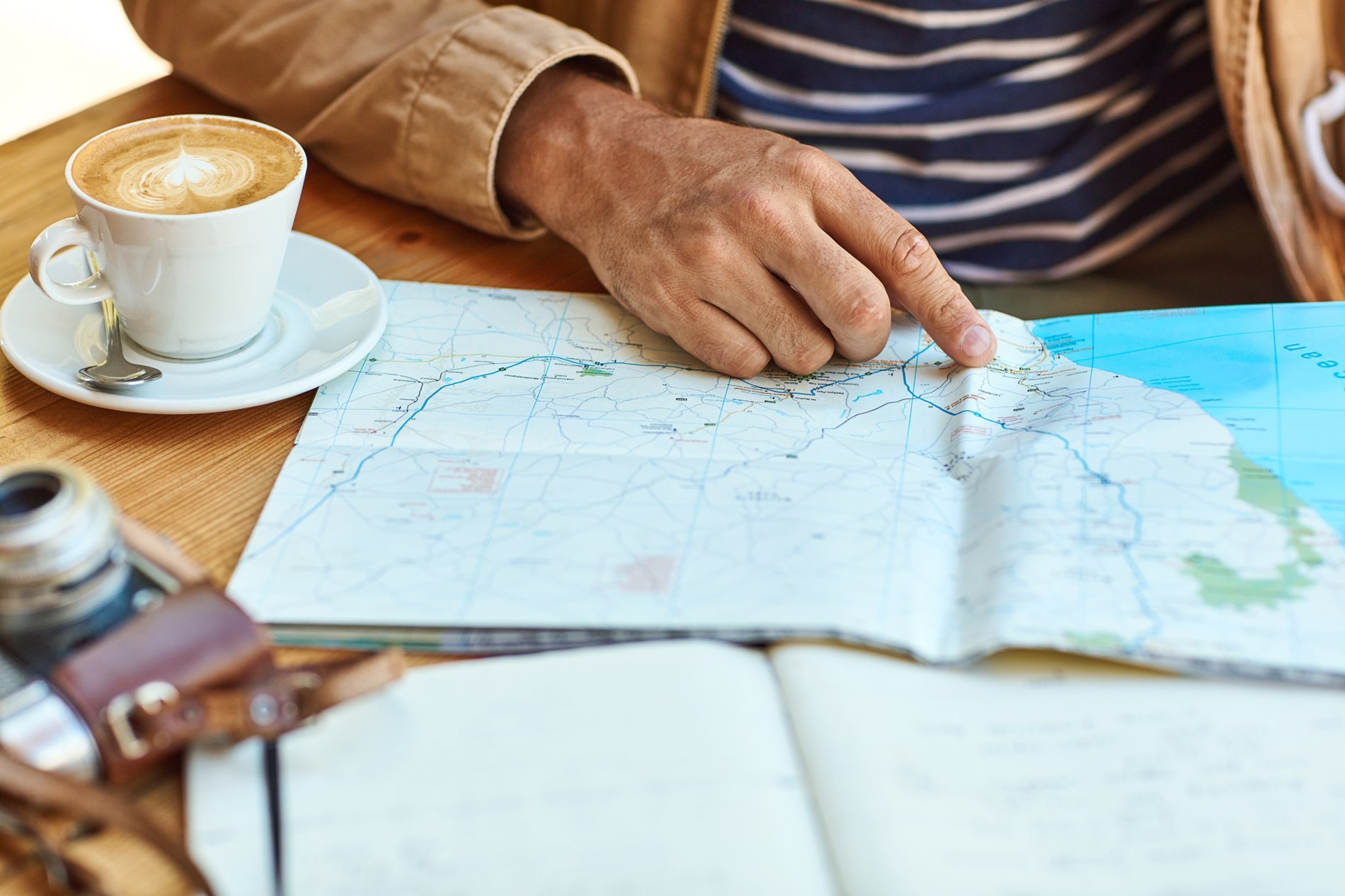 Un voyageur pointant une carte sur une table en bois avec un appareil photo et une tasse de café à côté, symbolisant la préparation d'un voyage.