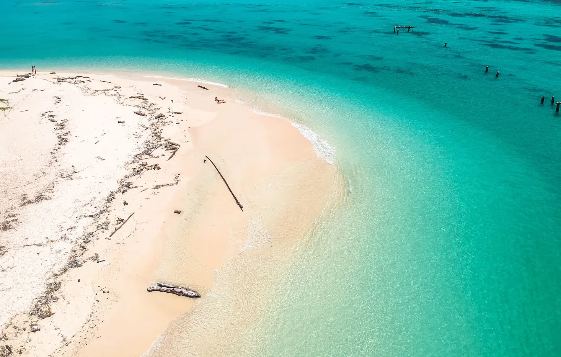 Vue aérienne d'une plage de sable blanc avec une mer turquoise à Koh Lipe, Thaïlande. Quelques personnes sont visibles au loin, profitant de la tranquillité de la plage isolée. 