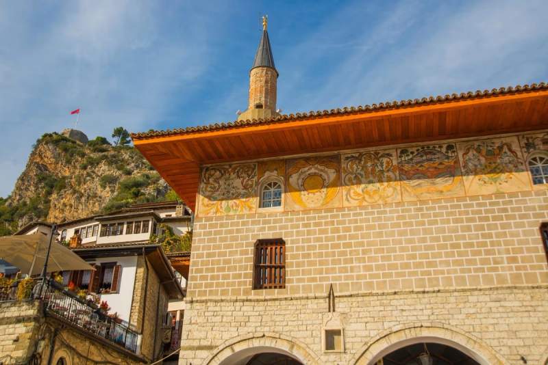 Vue de la mosquée de Berat avec ses fresques colorées et son minaret, sur fond de colline et drapeau albanais