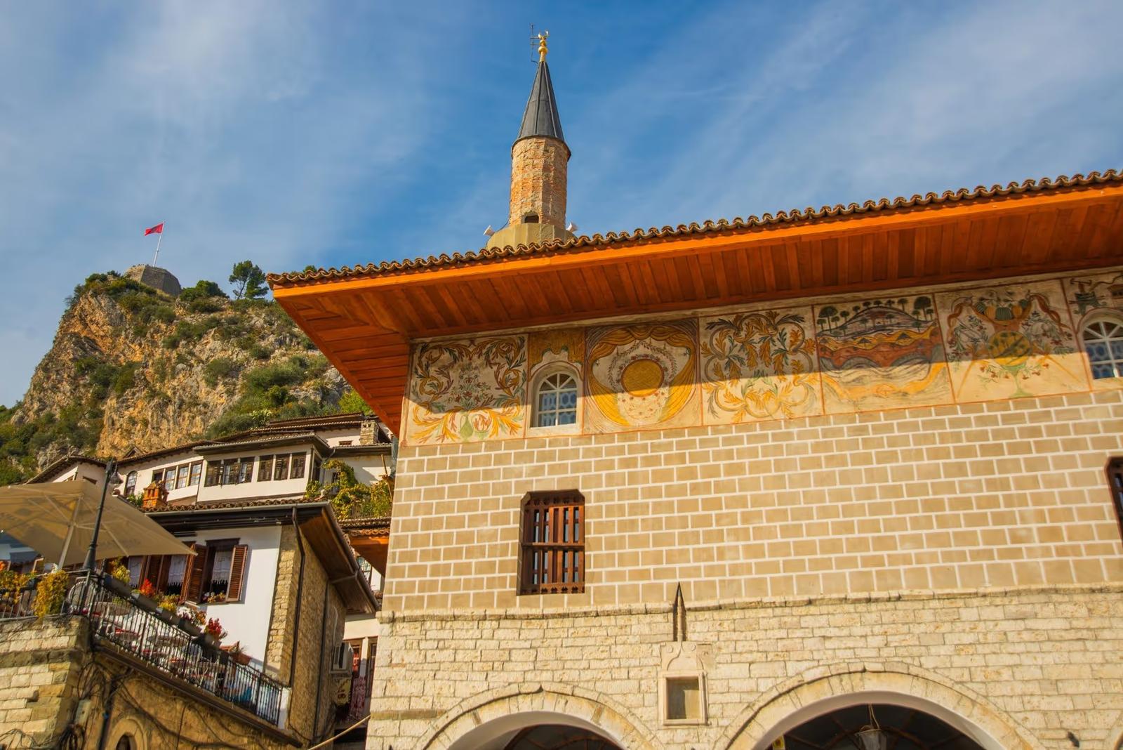 Vue de la mosquée de Berat avec ses fresques colorées et son minaret, sur fond de colline et drapeau albanais