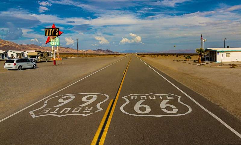 Marquage au sol Route 66 sur une route désertique avec le panneau néon de Roy's Motel & Cafe en arrière-plan
