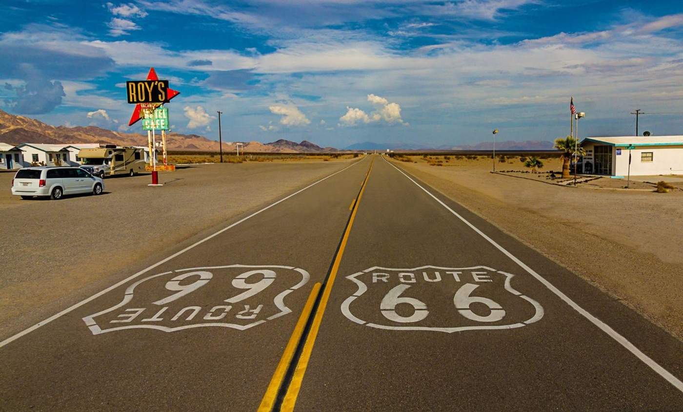 Marquage au sol Route 66 sur une route désertique avec le panneau néon de Roy's Motel & Cafe en arrière-plan
