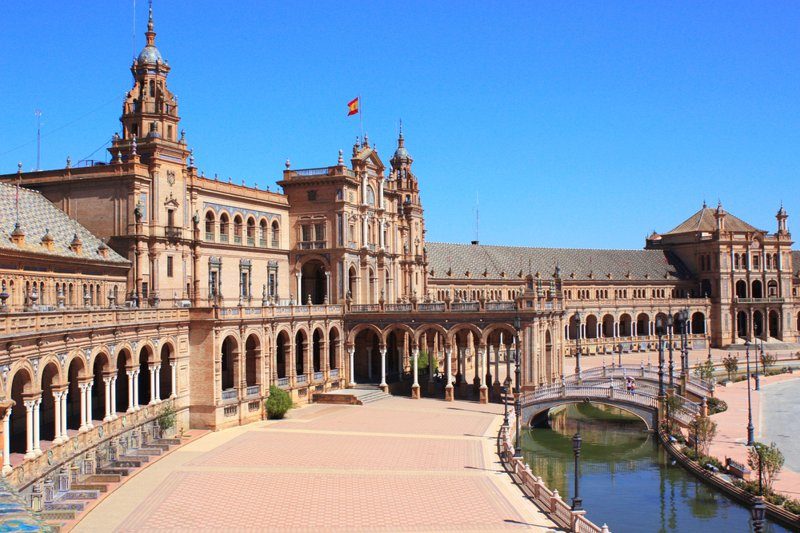 Vue panoramique de la Plaza de España à Séville avec son architecture en arcades, ses tours majestueuses et son canal traversé par des petits ponts.
