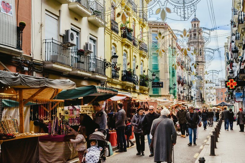 Rue animée du quartier Ruzafa à Valence, avec des stands de marché en plein air et des passants sous des décorations suspendues.