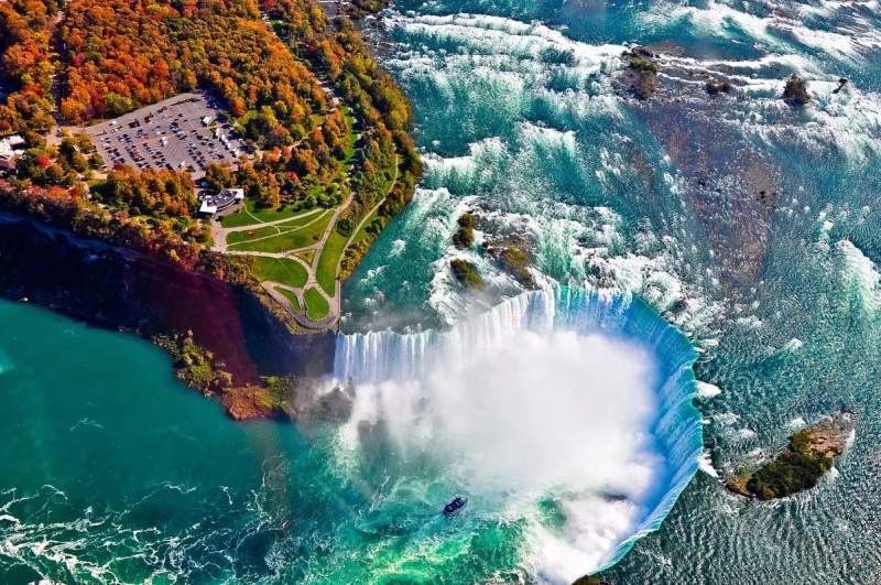Vue aérienne des chutes du Niagara avec des eaux tumultueuses, une brume dense et un parc verdoyant à proximité