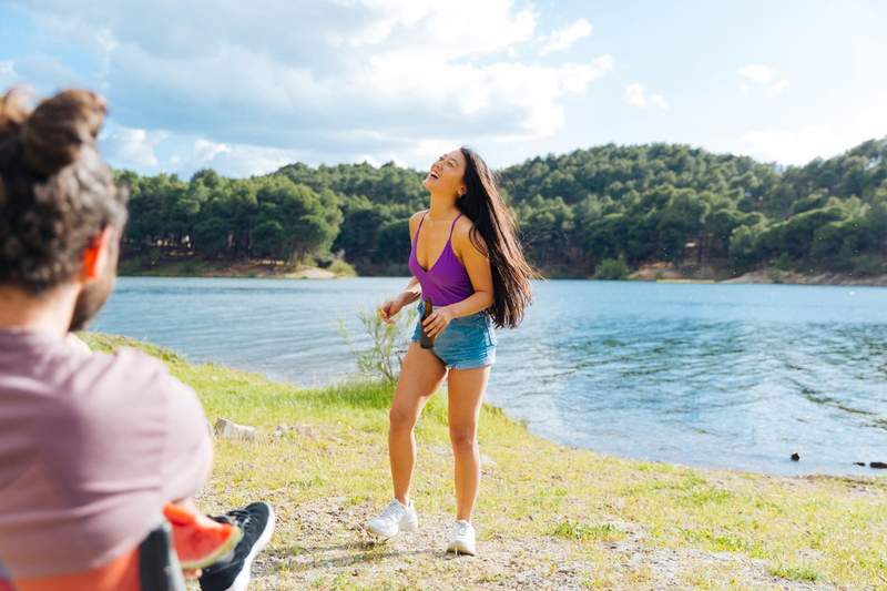 Jeune femme riant au bord d'un lac en France, entourée de forêt, lors d'un séjour d'été entre amis