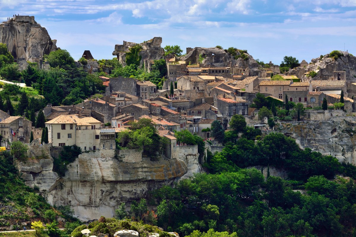 Vue panoramique du village perché des Baux-de-Provence, avec ses maisons en pierre, ses falaises blanches et la végétation des Alpilles en été