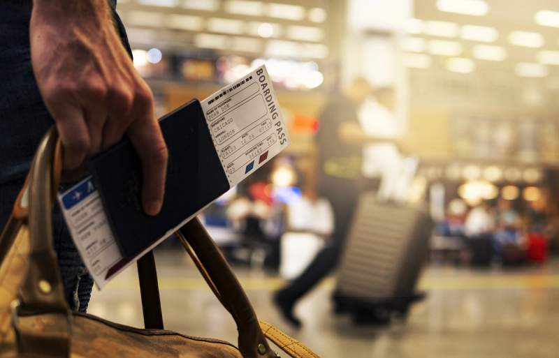 Une personne tient un passeport et une carte d’embarquement dans une main, tout en portant un sac de voyage dans l’autre.