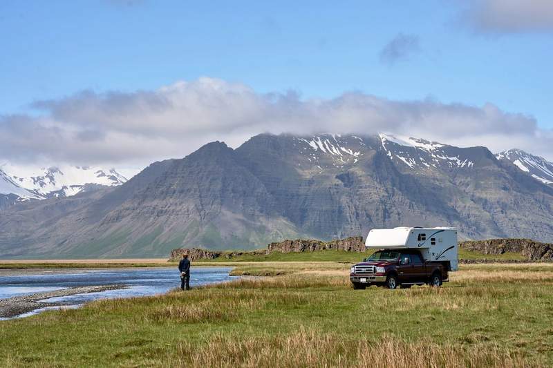 Camping-car 4x4 garé dans un paysage sauvage d'Islande avec montagnes enneigées en arrière-plan.