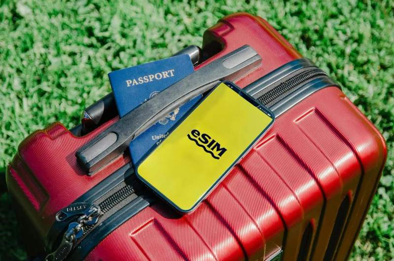 Valise rouge avec passeport et téléphone affichant 'eSIM', prêt pour le voyage.