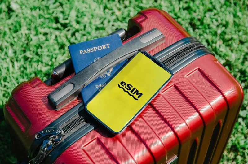 Valise rouge avec passeport et téléphone affichant 'eSIM', prêt pour le voyage.