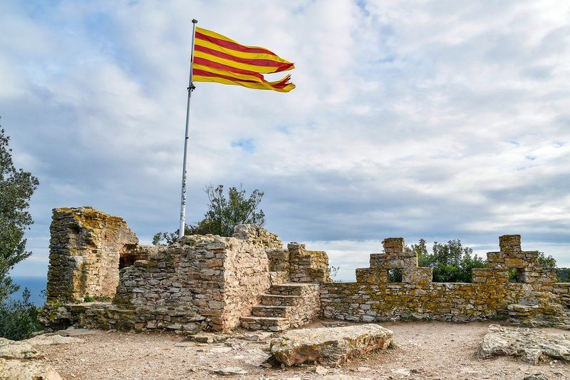 Ruines du château de Begur avec le drapeau catalan flottant, offrant une vue panoramique sur la Costa Brava.