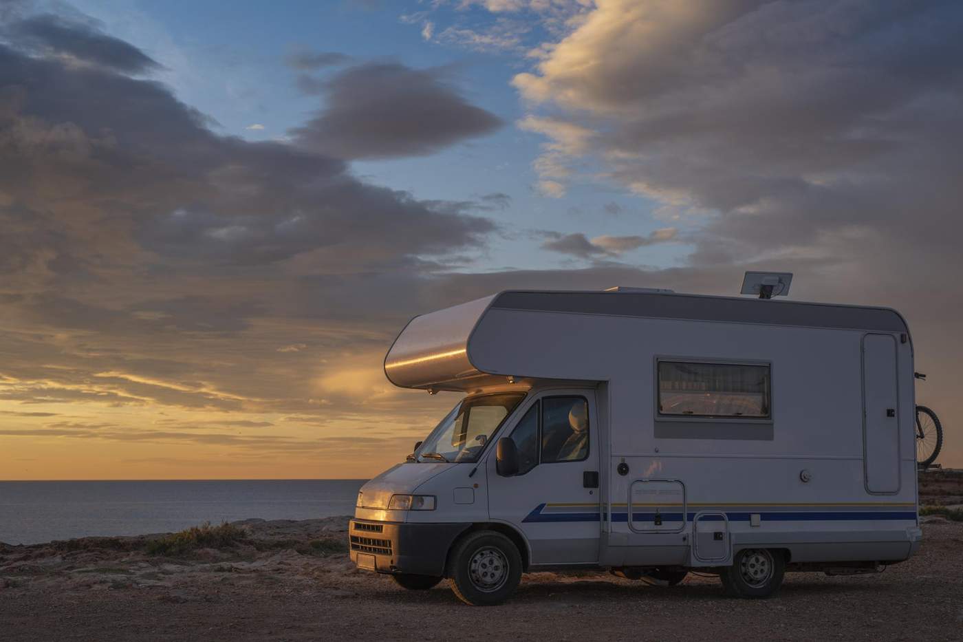 Camping-car stationné face à un coucher de soleil au bord de la mer en France.