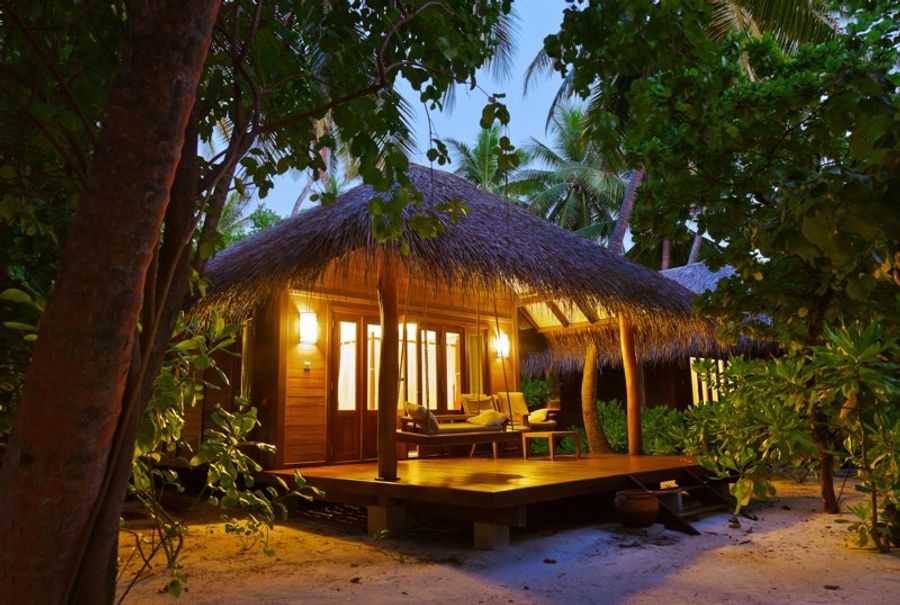 Bungalows en bois avec toits de chaume éclairés la nuit, entourés de végétation tropicale.
