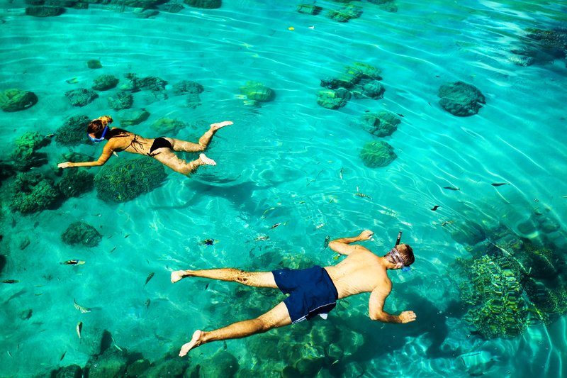 Deux voyageurs font du snorkeling dans les eaux turquoise des îles Perhentian, entourés de coraux et poissons tropicaux.