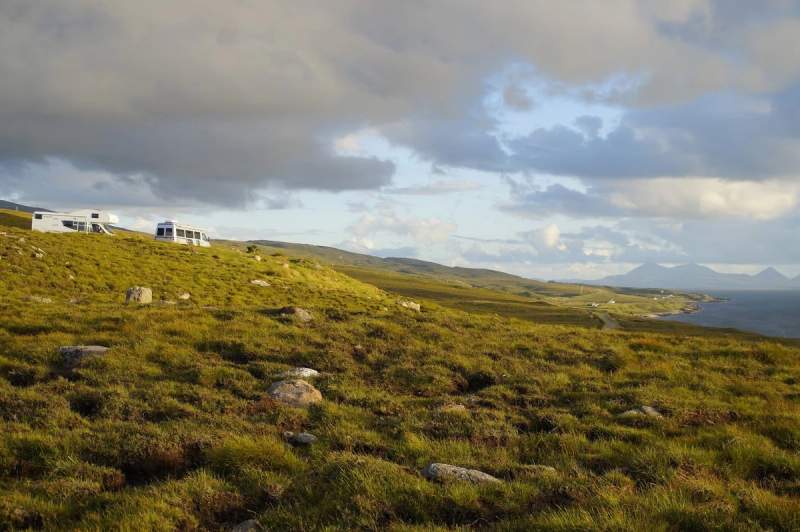 Camping-car stationné sur une colline verdoyante avec vue sur la mer en Écosse.