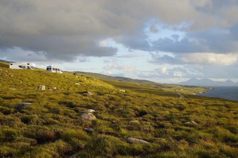 Camping-car stationné sur une colline verdoyante avec vue sur la mer en Écosse.