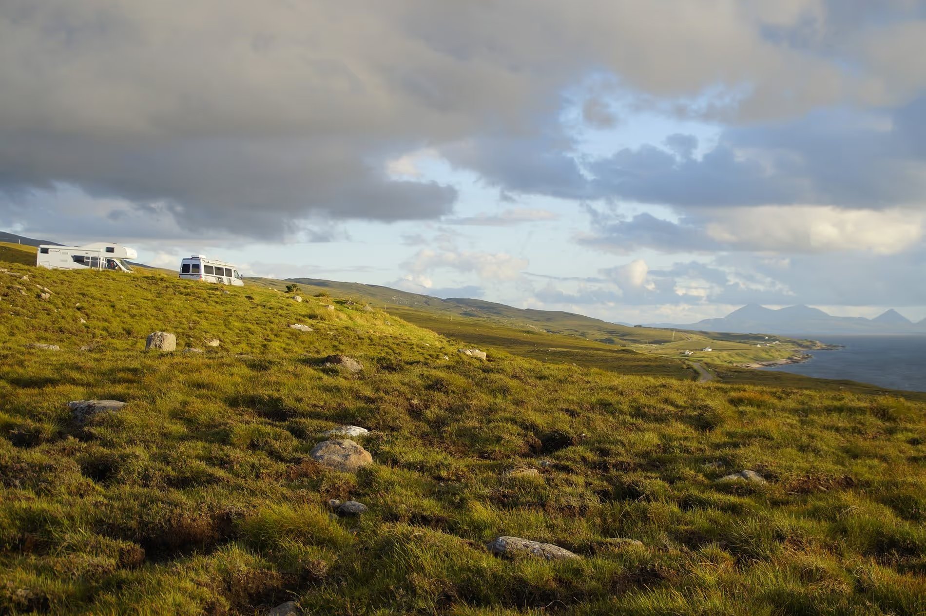 Camping-car stationné sur une colline verdoyante avec vue sur la mer en Écosse.