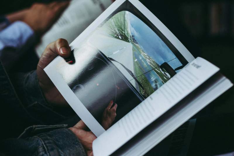 Personne lisant un livre ouvert montrant une photo de route avec un paysage.