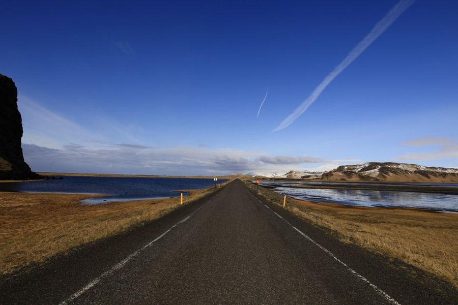Route droite et interminable en Islande bordée de lacs sous un ciel bleu, typique des road trips sur la Ring Road