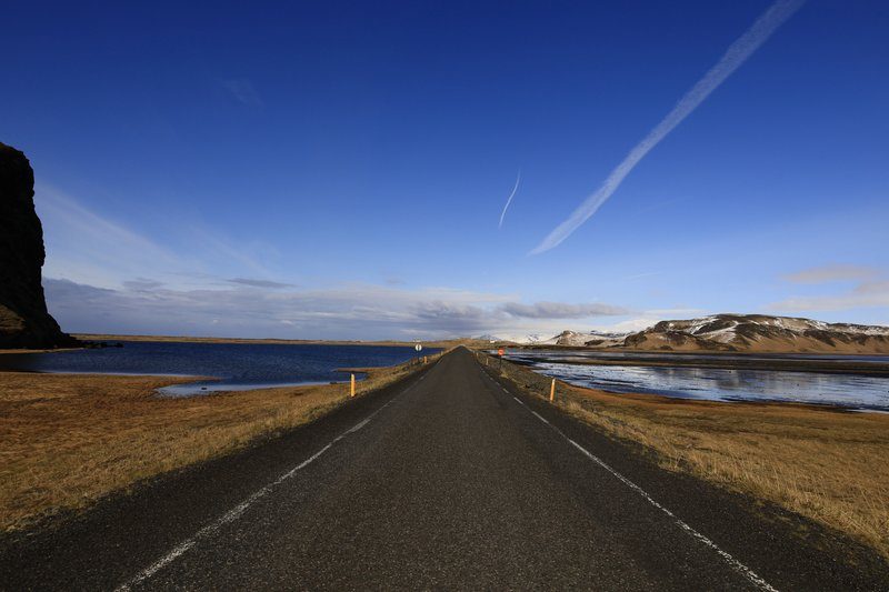 Route droite et interminable en Islande bordée de lacs sous un ciel bleu, typique des road trips sur la Ring Road