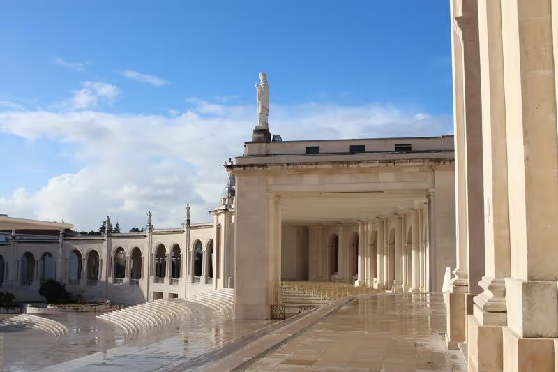 Vue partielle du sanctuaire de Fatima avec ses colonnes et ses statues sous un ciel bleu, Portugal.