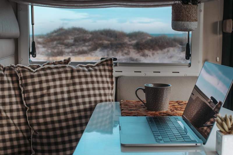 Espace de travail cosy dans un van avec ordinateur portable et tasse de café face à la mer.