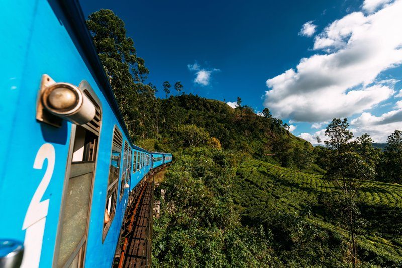 Train bleu emblématique du Sri Lanka traversant les plantations de thé et les montagnes, offrant une vue panoramique spectaculaire.