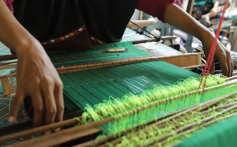Artisanat de tissage traditionnel avec des mains travaillant sur un métier à tisser et des fils colorés.