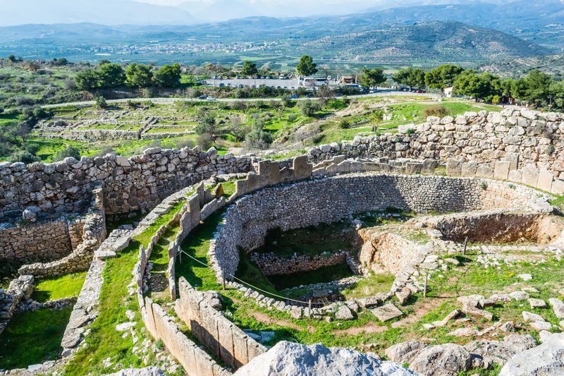 Ruines circulaires du site archéologique de Mycènes, avec vue sur les montagnes en arrière-plan.