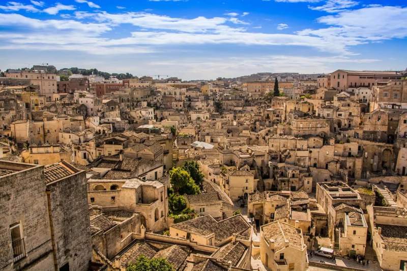 Vue panoramique des Sassi de Matera en Italie, avec ses maisons historiques en pierre sous un ciel bleu.
