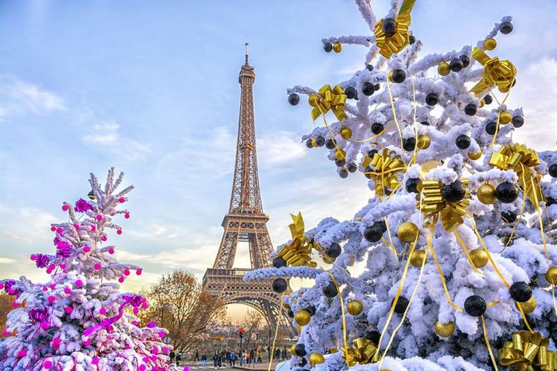 La tour Eiffel à Paris entourée de sapins de Noël décorés, sous un ciel d’hiver lumineux.