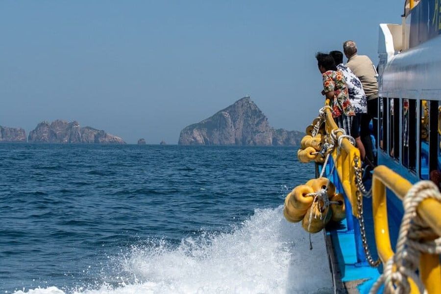 Des passagers profitant de la vue à bord d’un ferry en mer, avec des rochers visibles à l’horizon.